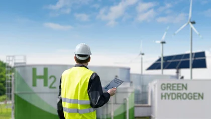 Man in a high-vis jacket looking away at wind turbines and storage containers
